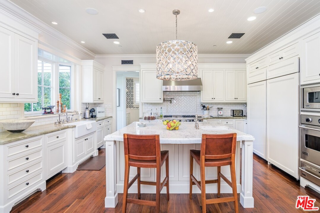 826 Greentree Road Pacific Palisades, CA 90272 - Photo 10 of 29 a kitchen with stainless steel appliances kitchen island granite countertop a dining table chairs and white cabinets