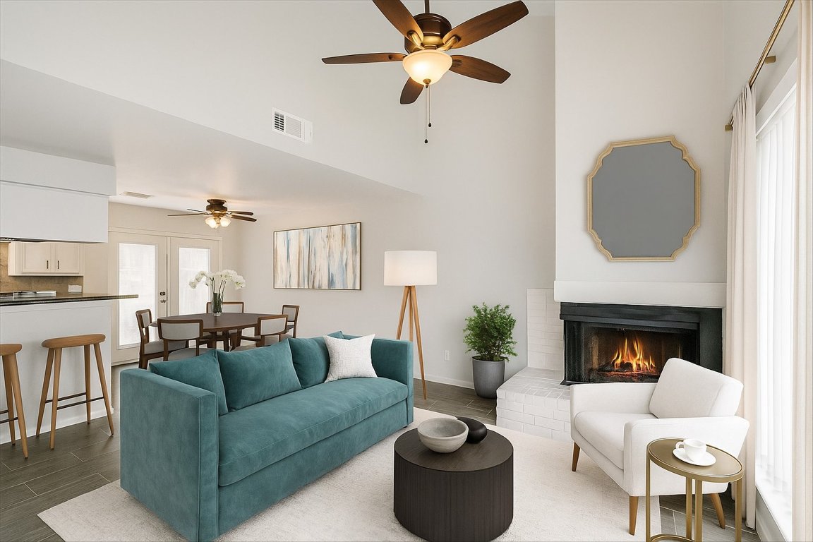 Living area with ceiling fan, a brick fireplace, wood tiled floors, and a towering ceiling