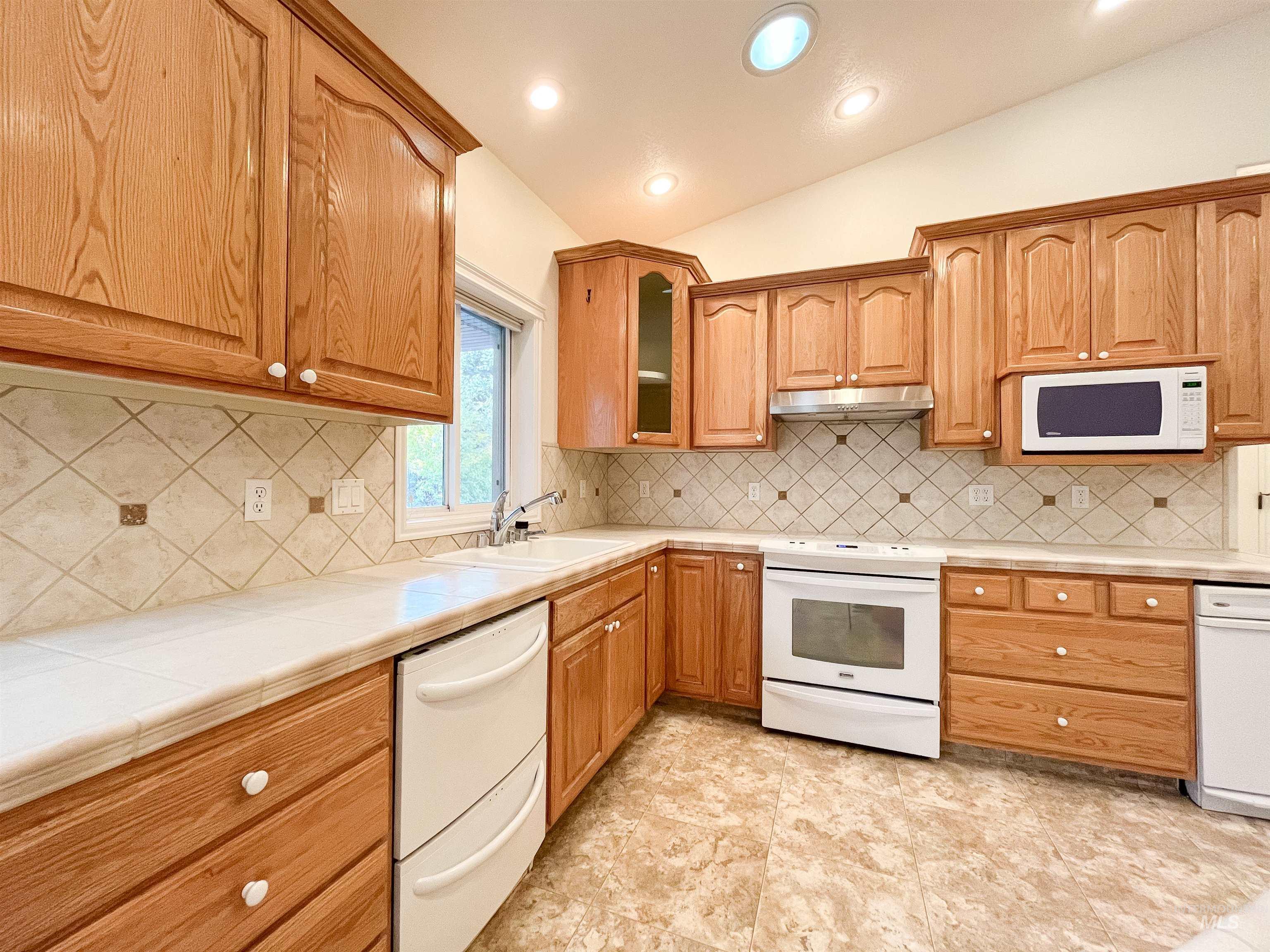 5231 North Morninggale Way Boise, ID 83713 - Photo 24 of 44 Kitchen featuring lofted ceiling, white appliances, glass insert cabinets, backsplash, and recessed lighting