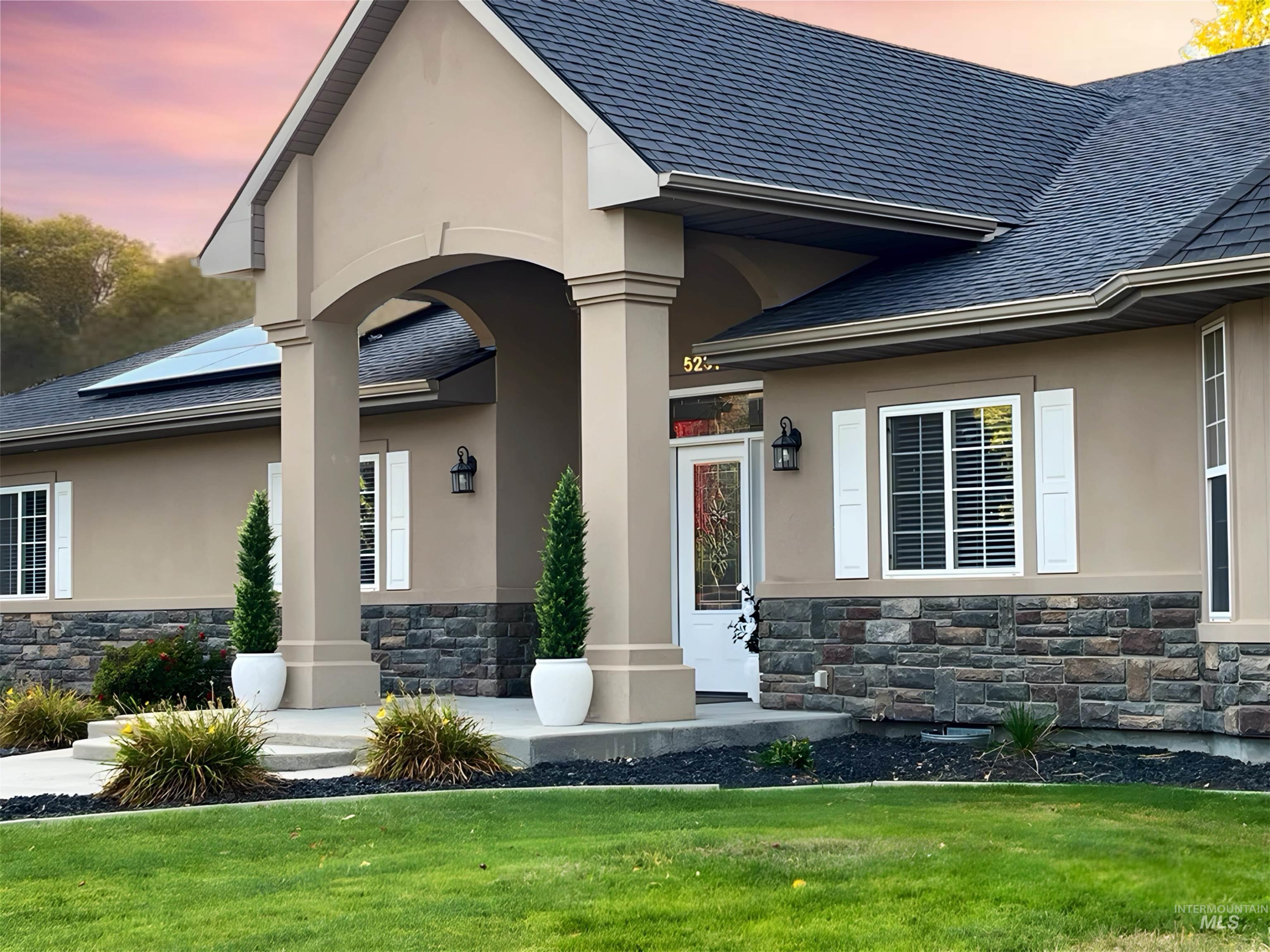 5231 North Morninggale Way Boise, ID 83713 - Photo 41 of 44 Exterior entry at dusk with stone siding, covered porch, a yard, stucco siding, and a shingled roof