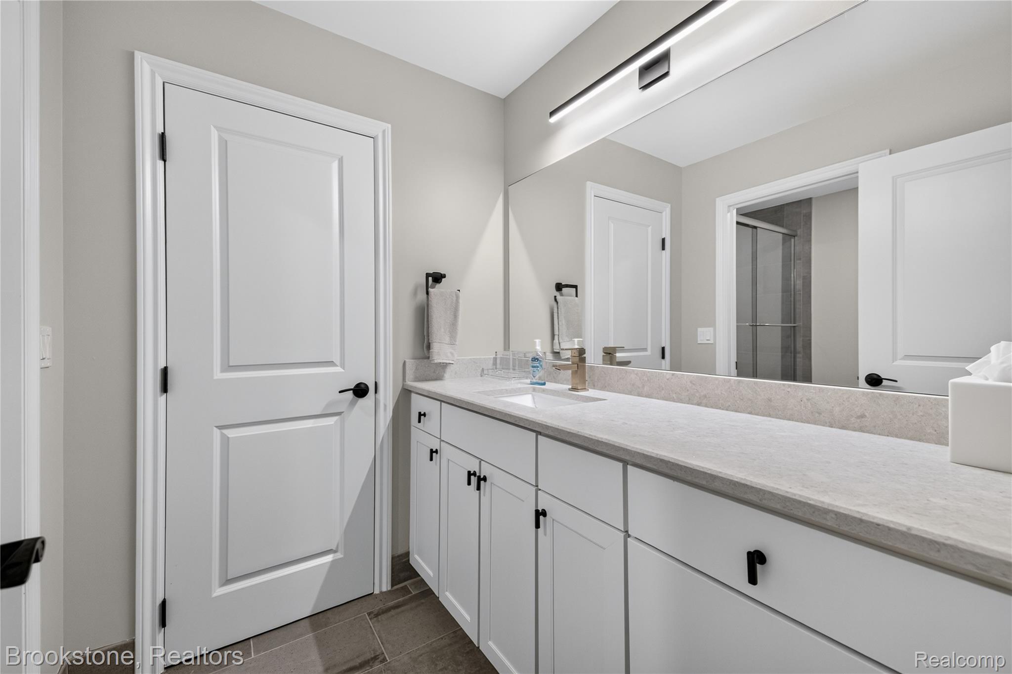 2167 Sanctuary Court Rochester, MI 48309 - Photo 56 of 68 Contemporary bathroom featuring a spacious vanity with white cabinetry, matte black hardware, a light-toned countertop, and a large wall-mounted mirror with integrated lighting
