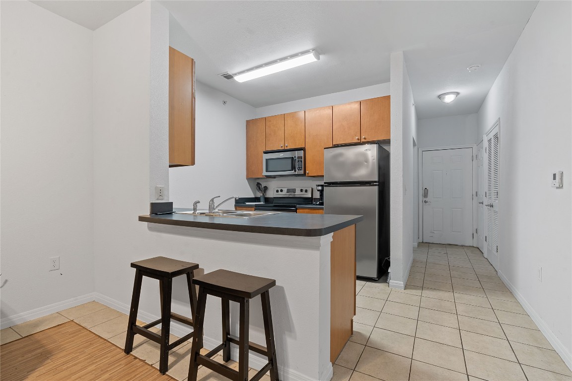 2515 Pearl Street, Unit 508 Austin, TX 78705 - Photo 17 of 25 Kitchen with light tile patterned floors, a breakfast bar area, dark countertops, a peninsula, and appliances with stainless steel finishes