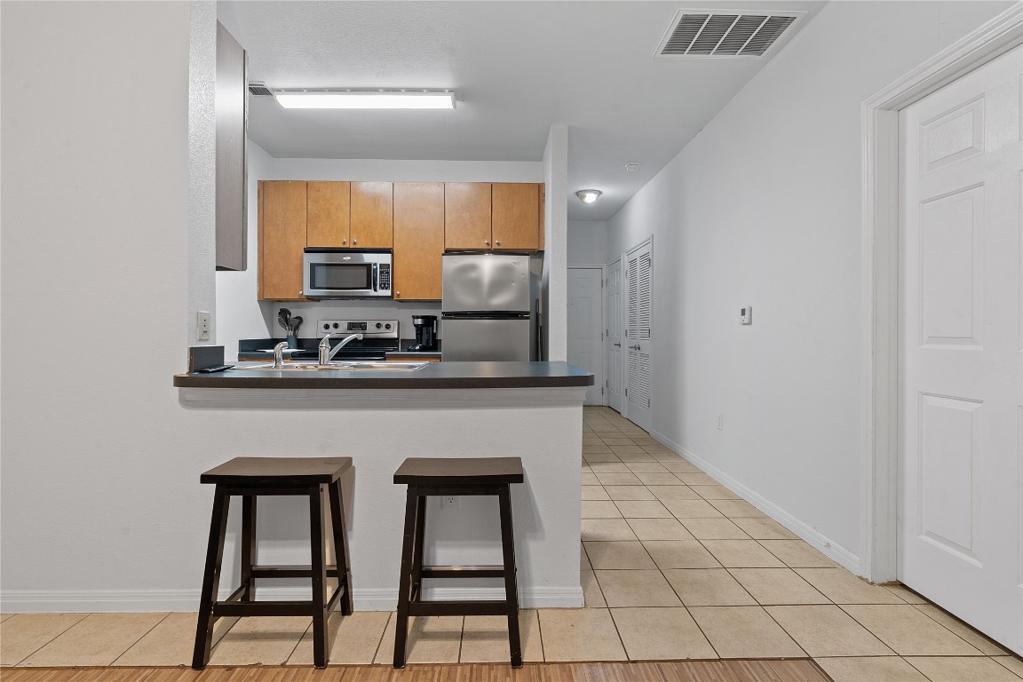 2515 Pearl Street, Unit 508 Austin, TX 78705 - Photo 18 of 25 Kitchen featuring a kitchen breakfast bar, appliances with stainless steel finishes, a peninsula, and light tile patterned floors