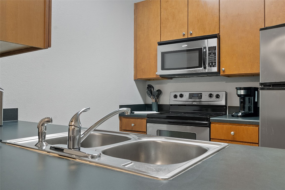 2515 Pearl Street, Unit 508 Austin, TX 78705 - Photo 19 of 25 Kitchen featuring stainless steel appliances, brown cabinetry, dark countertops, and a textured wall