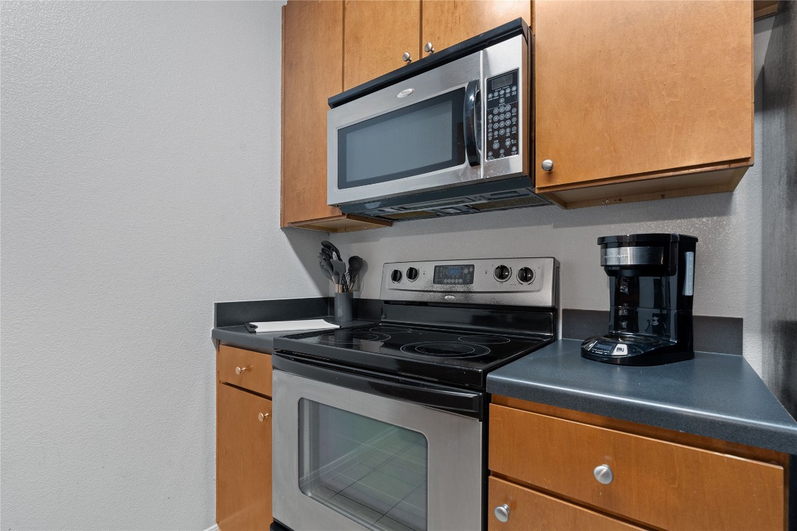 2515 Pearl Street, Unit 508 Austin, TX 78705 - Photo 21 of 25 Kitchen featuring dark countertops, appliances with stainless steel finishes, brown cabinetry, and a textured wall