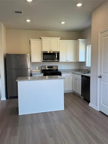 a kitchen with kitchen island granite countertop a sink a stove a refrigerator cabinets and wooden floor