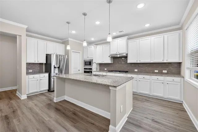 a large kitchen with stainless steel appliances kitchen island granite countertop a stove a sink and white cabinets with wooden floor