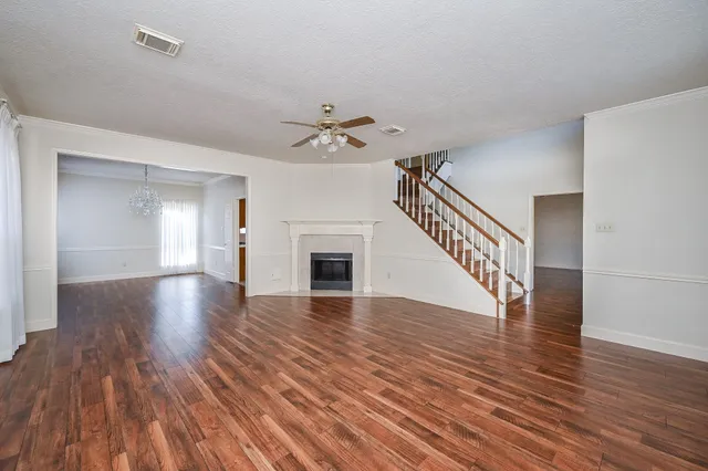 a view of an empty room with wooden floor and a ceiling fan