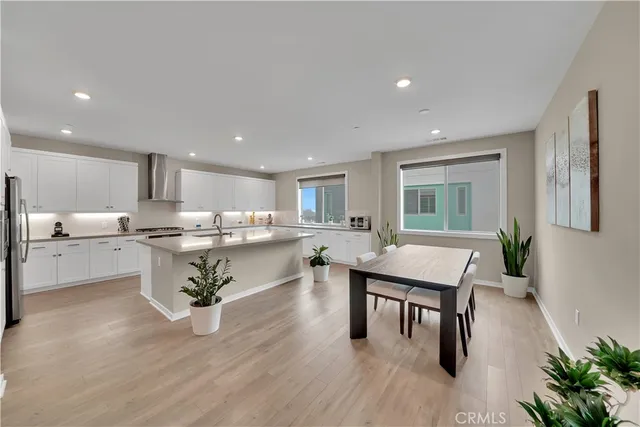 a room with stainless steel appliances a dining table wooden floor and a kitchen view