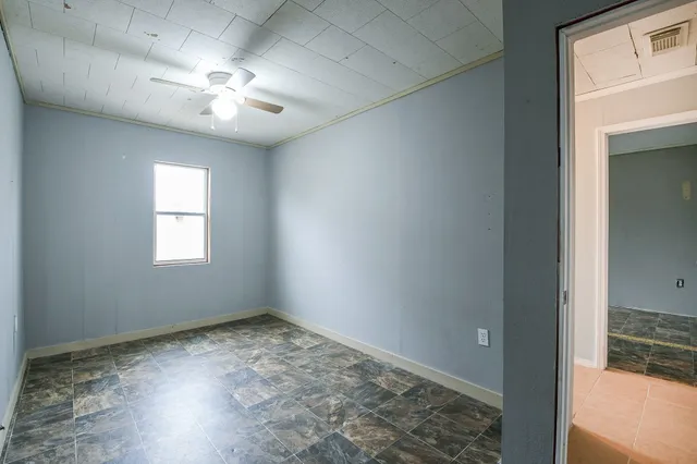 an empty room with a chandelier fan and windows