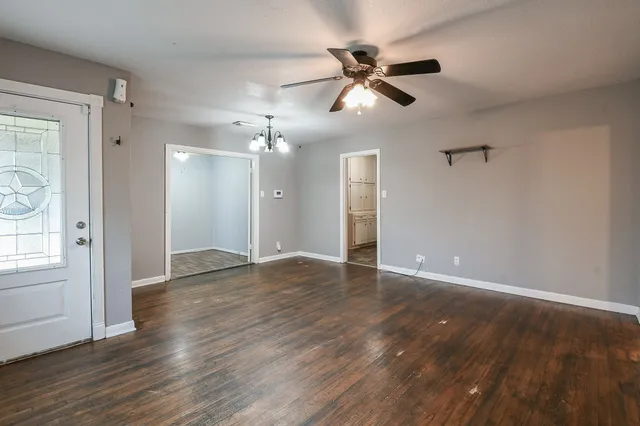 a view of an empty room with wooden floor and a ceiling fan