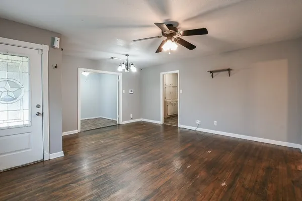 a view of an empty room with wooden floor and a ceiling fan