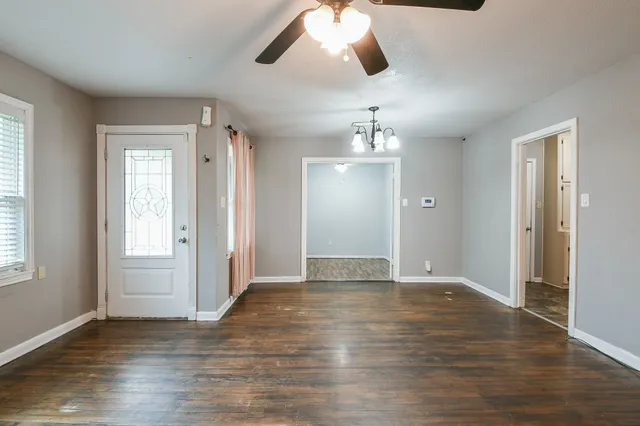 an empty room with wooden floor chandelier and windows