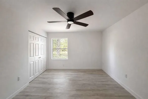 an empty room with wooden floor fan and windows