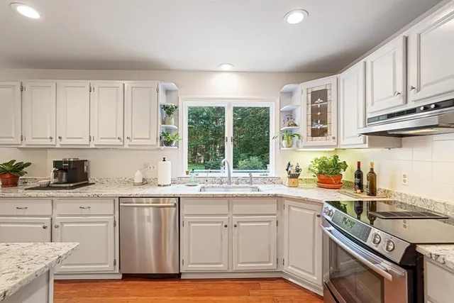 a kitchen with stainless steel appliances granite countertop a stove a sink dishwasher and white cabinets with wooden floor