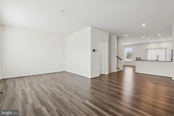 a view of an empty room with wooden floor and a kitchen