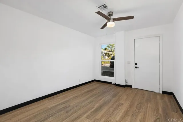 an empty room with wooden floor ceiling fan and windows