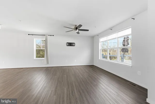 an empty room with wooden floor chandelier fan and windows