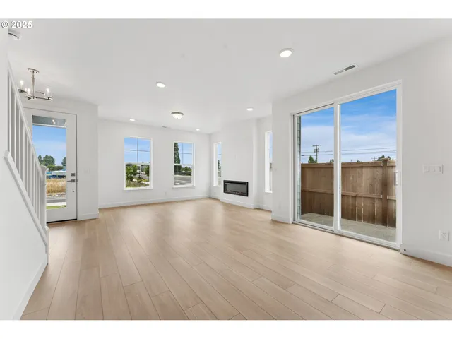 a view of an empty room with wooden floor and kitchen view