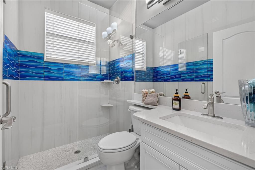 9970 Rookery Circle Estero, FL 33928 - Photo 23 of 50 Glass-enclosed shower with pebble-finish flooring and patterned blue accent tile