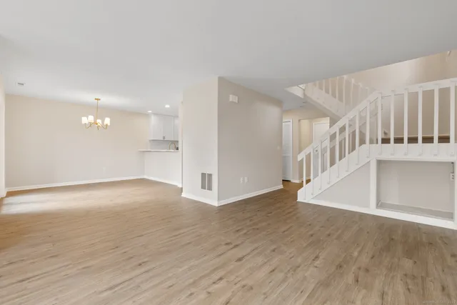 a view of an empty room with wooden floor and a kitchen