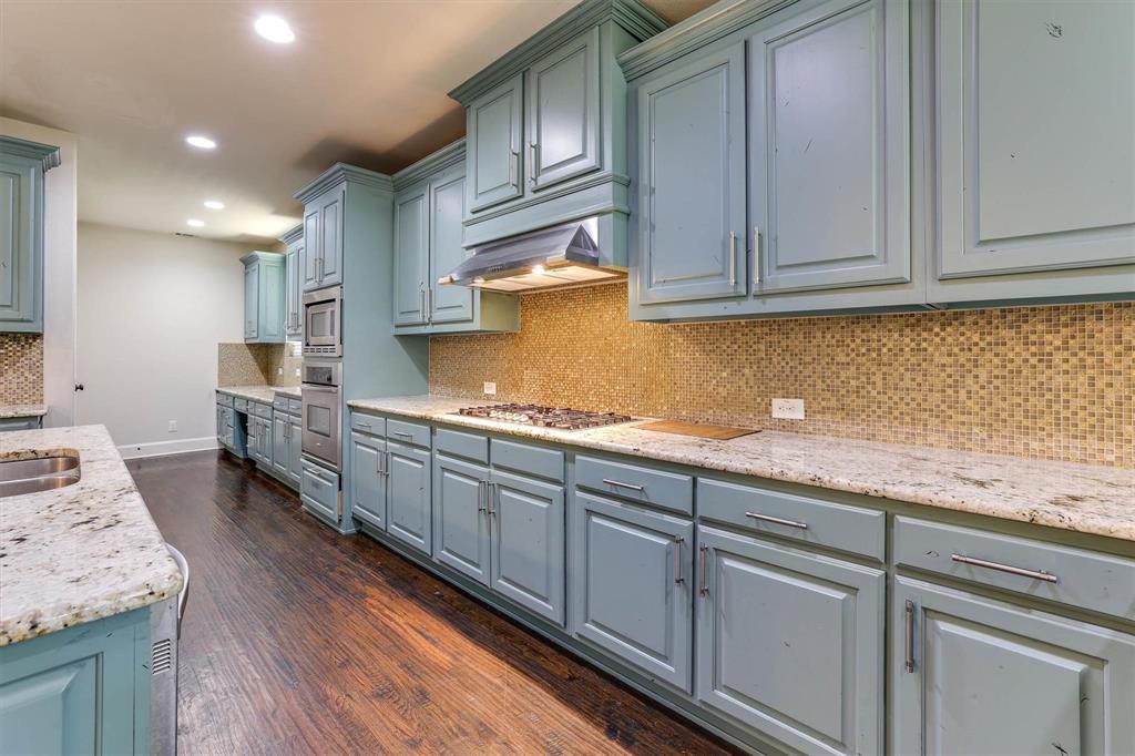 419 Rio Grande Drive Irving, TX 75039 - Photo 11 of 29 Kitchen featuring extensive light blue cabinetry, speckled stone countertops, a mosaic tile backsplash, built-in stainless steel appliances, and dark wood-finish flooring