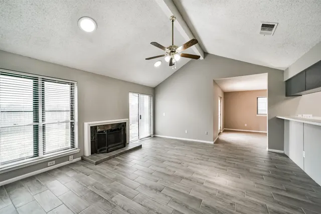 an empty room with windows fireplace and a kitchen view
