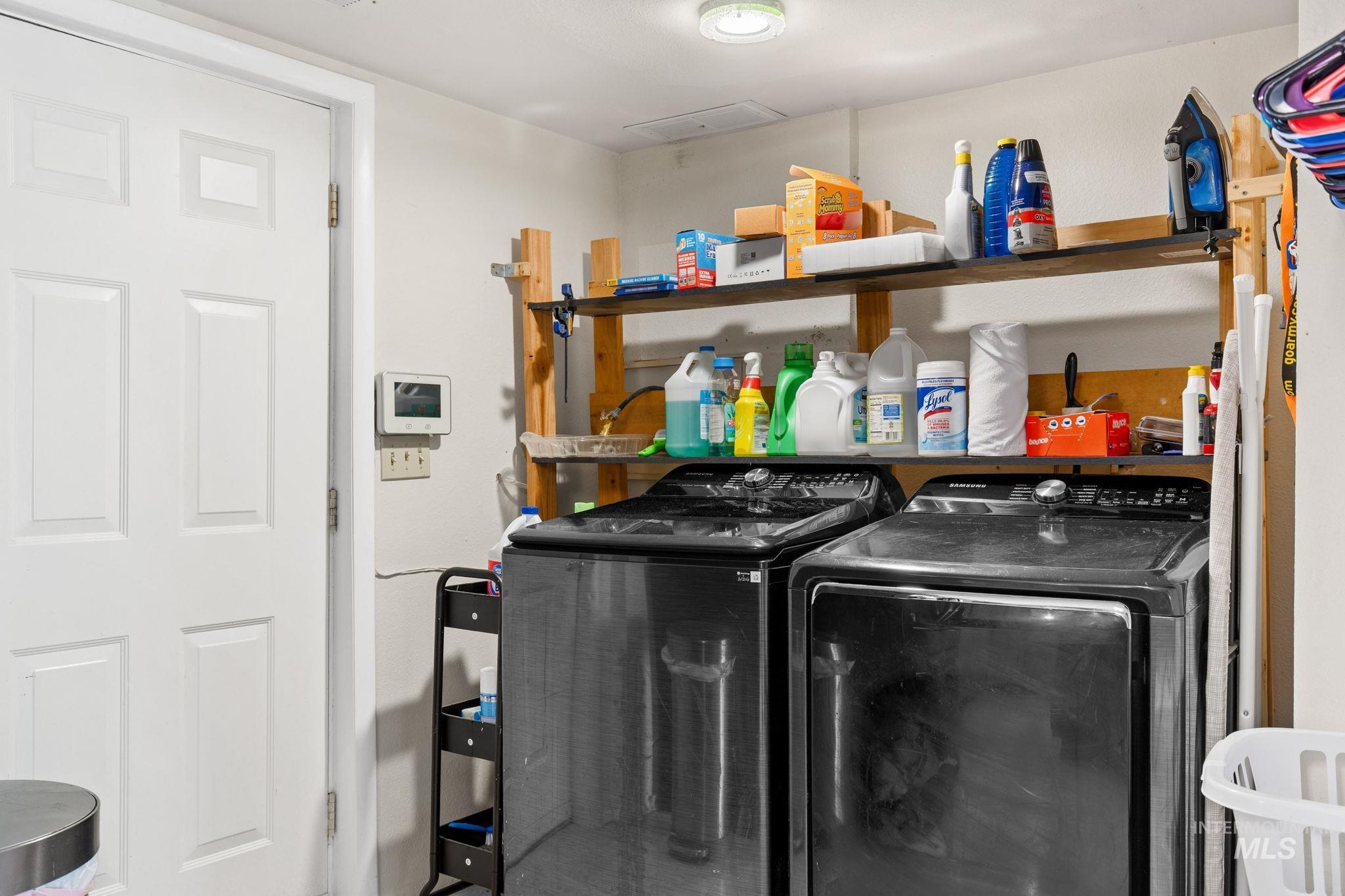 18338 Pride Lane Caldwell, ID 83607 - Photo 15 of 50 Dedicated laundry area featuring a white paneled door, built-in wooden shelving, and two dark-toned front-loading appliances