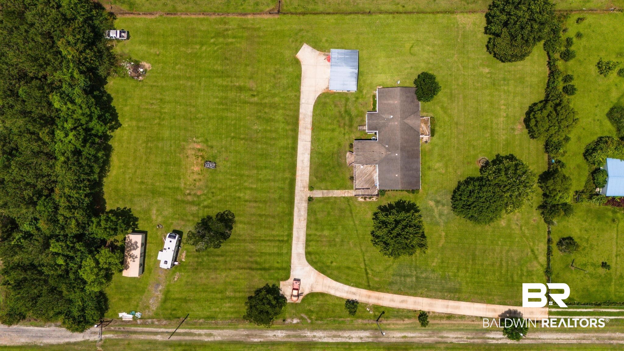 34985b Spring Road South, Unit B Stapleton, AL 36578 - Photo 7 of 31 Expansive property featuring a single-story residence with an attached garage, a long paved driveway, a separate outbuilding with a metal roof, and mature trees across a substantial green lawn