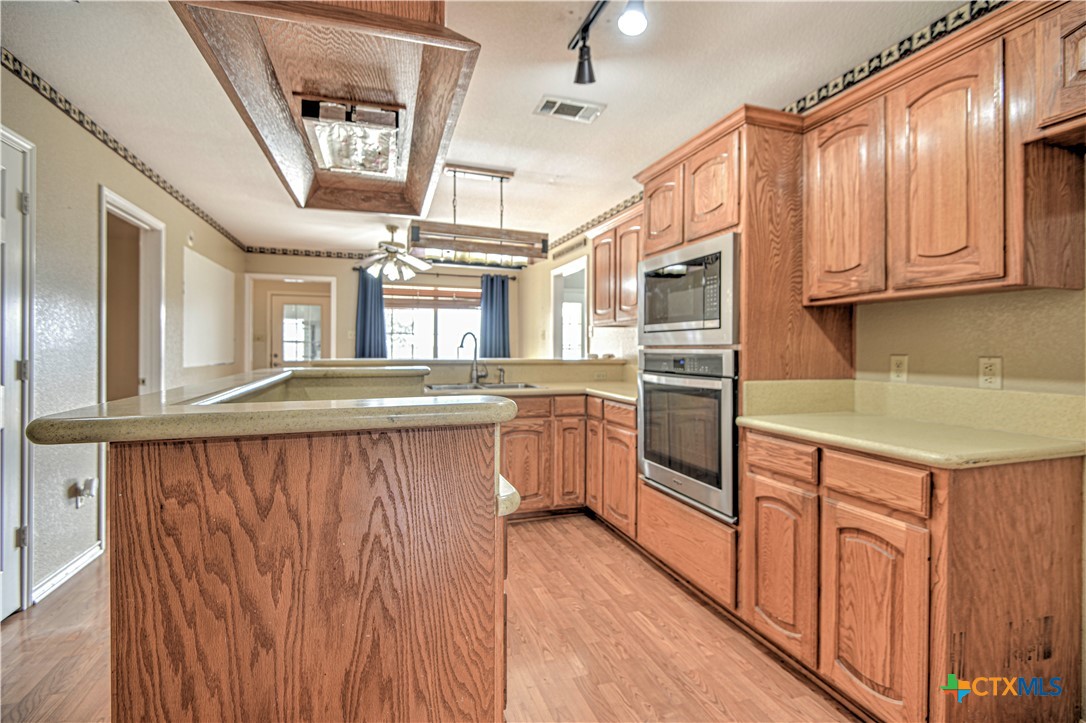 809 Hudson Lane Eddy, TX 76524 - Photo 15 of 48 a kitchen with kitchen island granite countertop a stove top oven a sink dishwasher and wooden cabinets with wooden floor