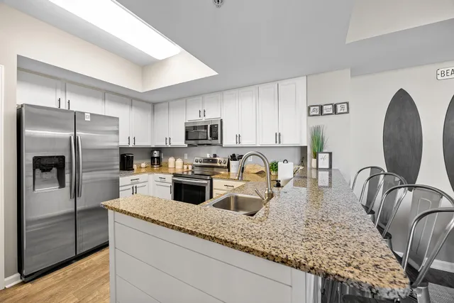 a kitchen with stainless steel appliances granite countertop a stove top oven a sink dishwasher a refrigerator and cabinets with wooden floor