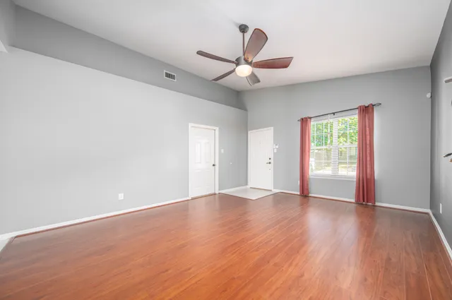 an empty room with wooden floor ceiling fan and windows