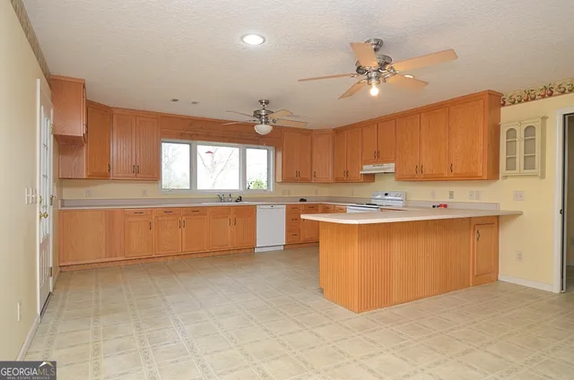a large kitchen with kitchen island granite countertop a stove a sink a refrigerator and white cabinets