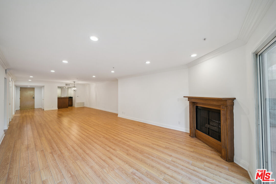 a view of an empty room with wooden floor kitchen and a window