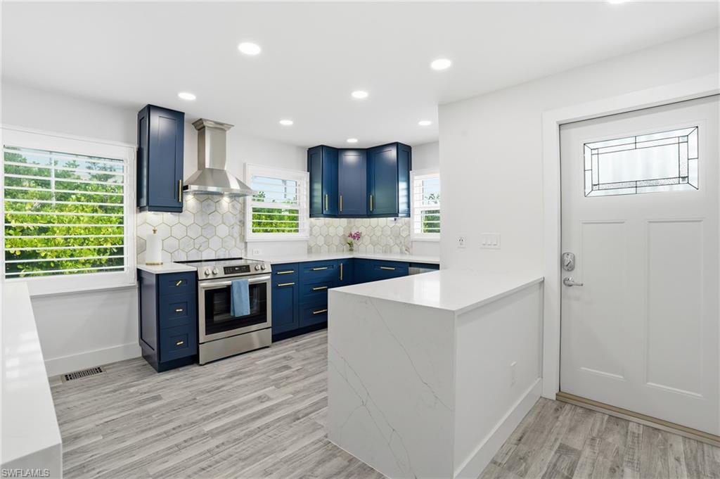 270 Dundee Road Fort Myers Beach, FL 33931 - Photo 15 of 48 Kitchen with wall chimney exhaust hood, stainless steel electric range, a peninsula, blue cabinets, and light stone countertops - Virtually Edited Image