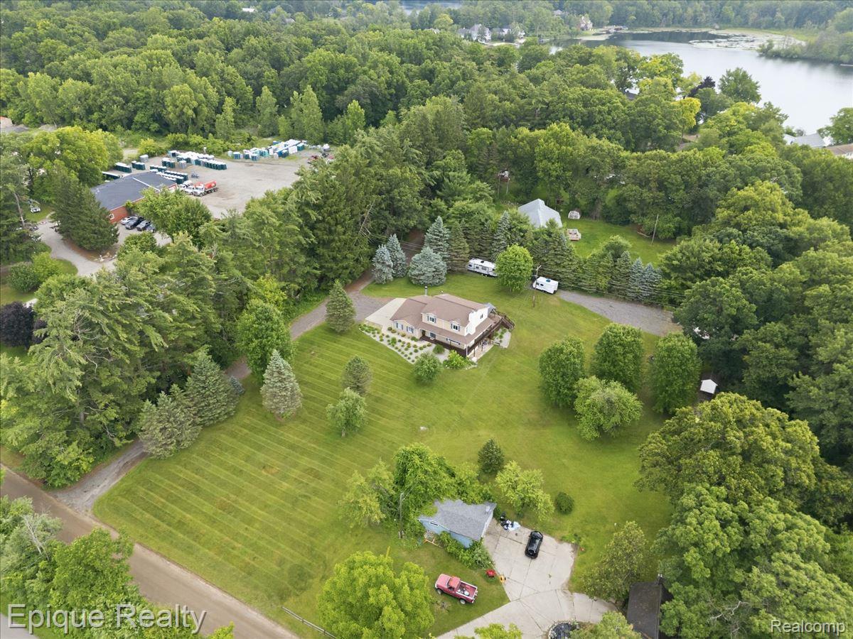 1221 Rhodes Road Lake Orion, MI 48360 - Photo 62 of 72 Expansive property featuring a two-story residence with a multi-level deck, substantial green lawn areas, mature trees, and a visible body of water