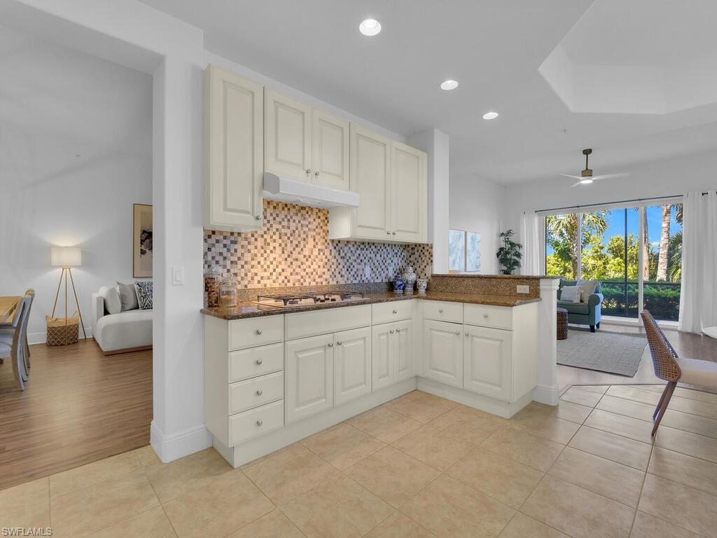 2710 Callista Court, Unit 104 Naples, FL 34114 - Photo 43 of 43 Kitchen with stainless steel gas stovetop, decorative backsplash, dark stone counters, under cabinet range hood, and open floor plan