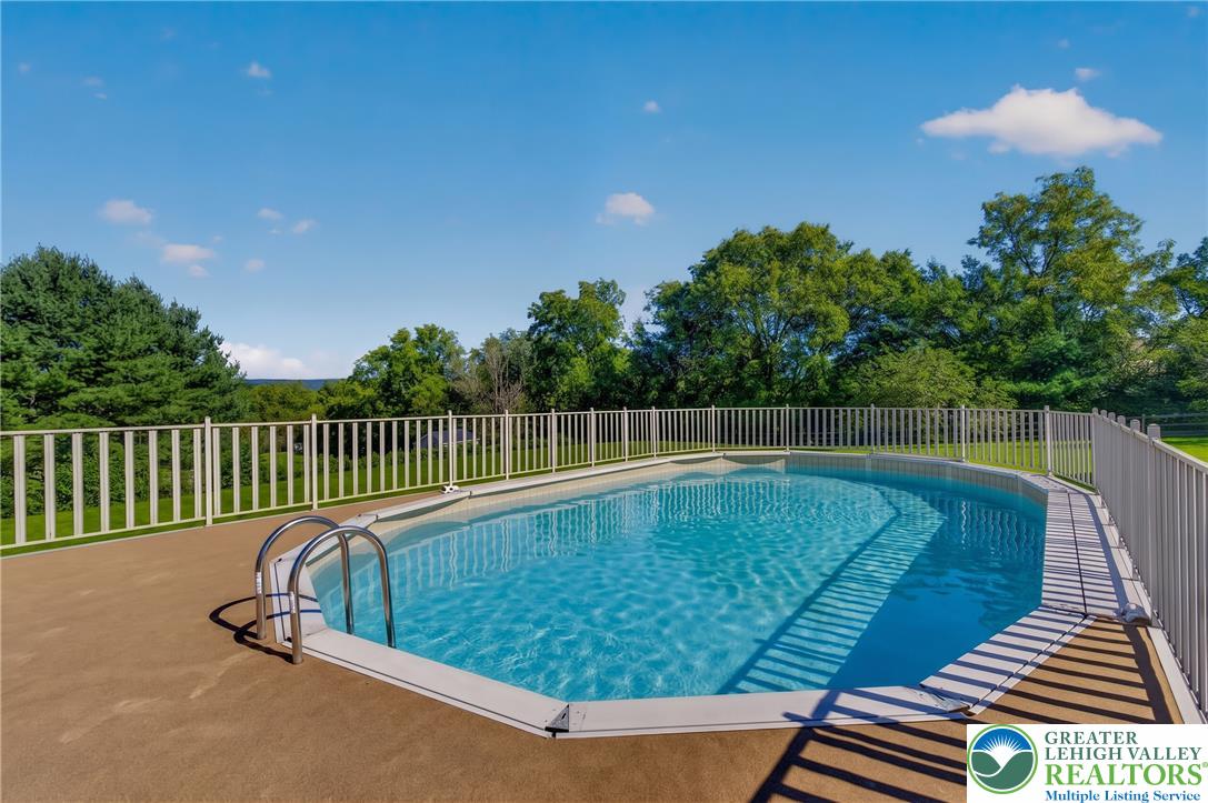 630 Clearfield Road Nazareth, PA 18064 - Photo 97 of 100 An inviting swimming pool is enclosed by safety fencing, surrounded by lush green trees.