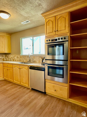 255 West Main Street Mount Pleasant, UT 84647 - Photo 16 of 35 Kitchen featuring light wood cabinetry, stainless steel double wall ovens, a coordinating dishwasher, wood-finish flooring, and a patterned tile backsplash