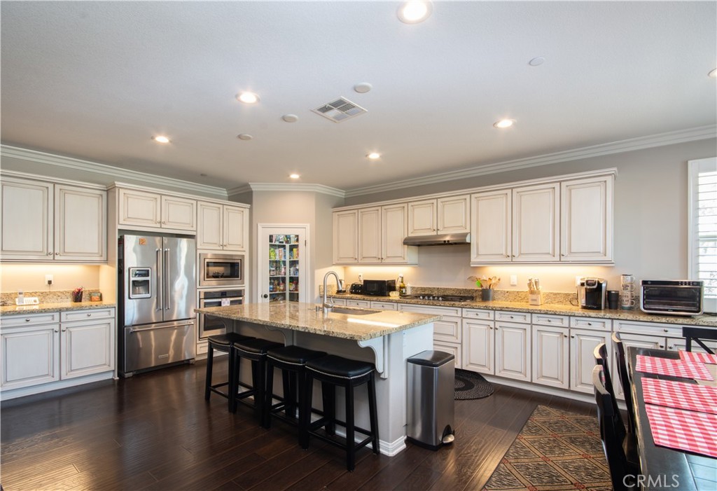 11950 Flicker Cove Corona, CA 92883 - Photo 3 of 28 a kitchen with stainless steel appliances granite countertop a table chairs sink refrigerator and cabinets