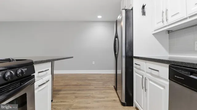 a kitchen with stainless steel appliances granite countertop a refrigerator a sink dishwasher a stove and white cabinets with wooden floor