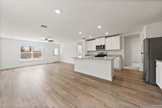 a kitchen with stainless steel appliances granite countertop a refrigerator microwave and white cabinets with wooden floor