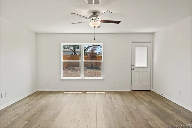 an empty room with wooden floor ceiling fan and windows