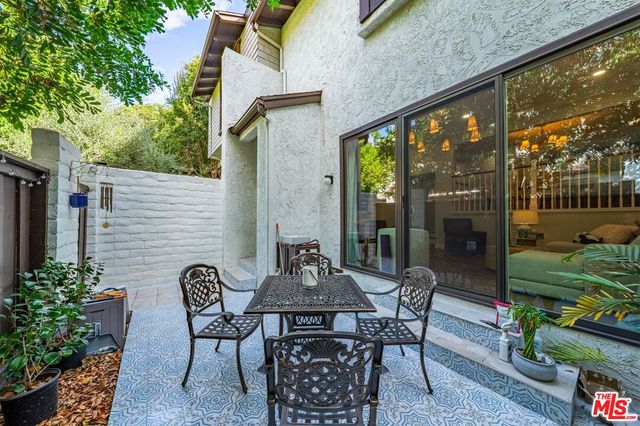 a view of a patio with table and chairs potted plants and floor to ceiling window