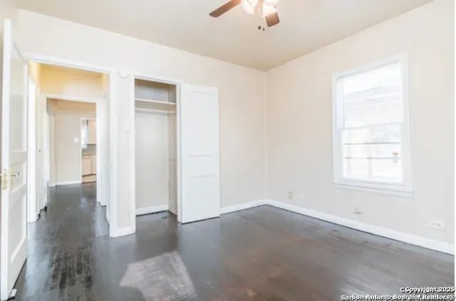 an empty room with chandelier fan and windows