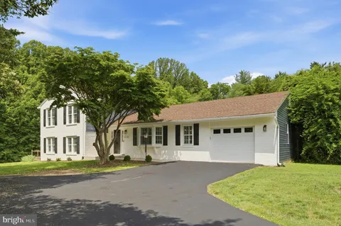 a view of a white house with a yard plants and large tree