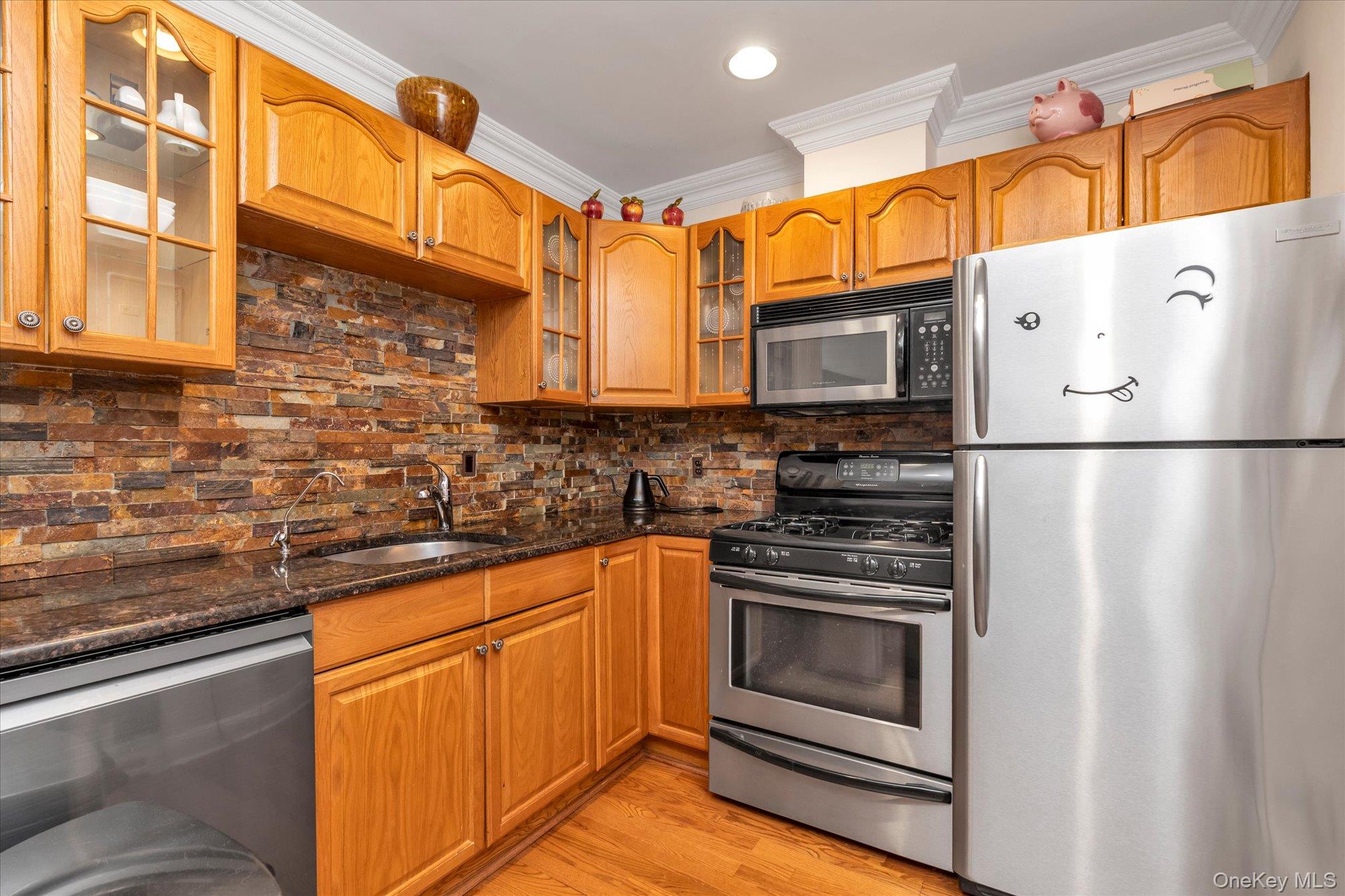 150 I U Willets Road Albertson, NY 11507 - Photo 11 of 21 Kitchen featuring wood cabinetry, dark speckled countertops, stone-look tile backsplash, stainless steel appliances, and wood-finish flooring