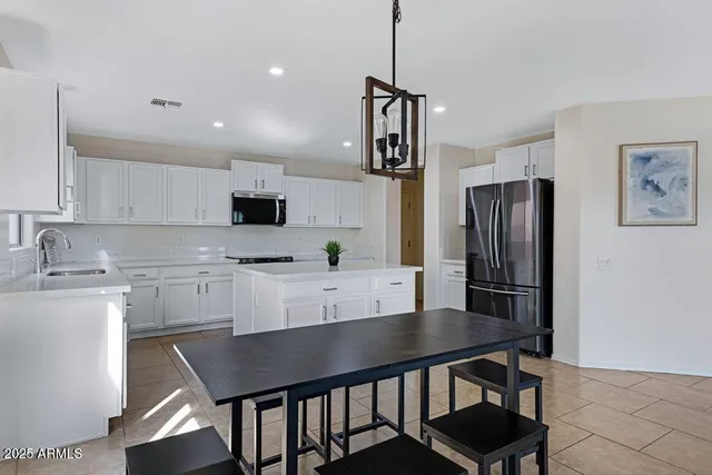 a kitchen with kitchen island granite countertop a table chairs refrigerator and white cabinets