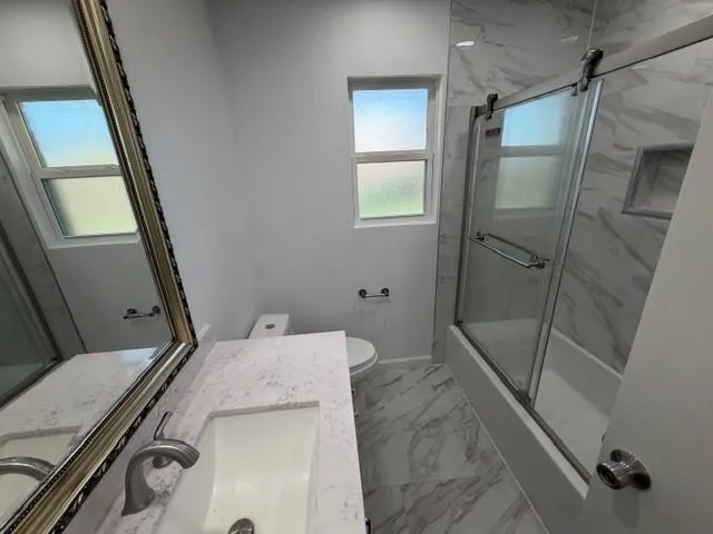 a bathroom with a granite countertop sink a toilet a shower and vanity