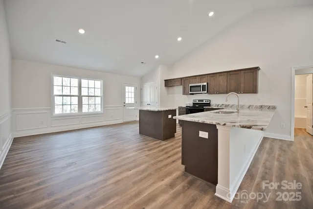 a kitchen with stainless steel appliances granite countertop a refrigerator a sink dishwasher a stove top oven a refrigerator and white cabinets with wooden floor